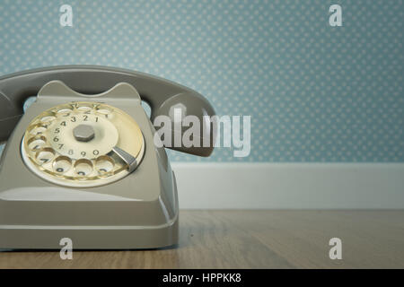 Gray vintage phone on hardwood floor and dotted light blue wallpaper on background. Stock Photo