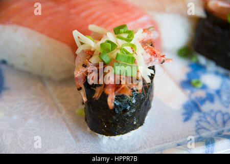 Intricate sushi shown with ginger and chives, in focus, with salmon sashimi in soft focus in background, and displayed on a plate with a Japanese desi Stock Photo