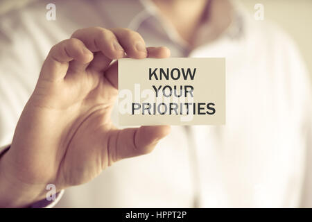 Closeup on businessman holding a card with text KNOW YOUR PRIORITIES, business concept image with soft focus background and vintage tone Stock Photo