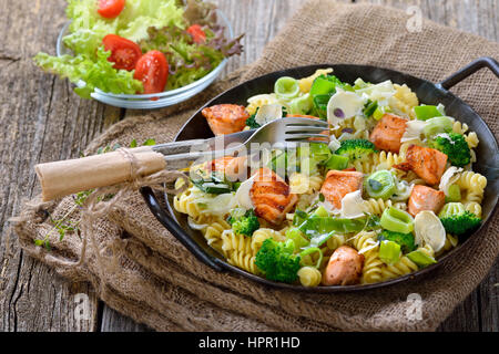 Italian pasta with fried cuts of salmon fillet, horseradish and a sauce of cream and leek served in an iron frying pan with a side salad Stock Photo