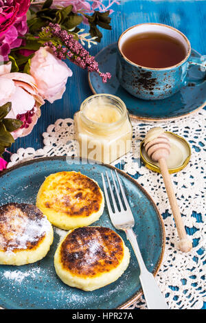 Cottage cheese fritters, honey and tea in a vintage cup on a blue background. Studio Photo Stock Photo