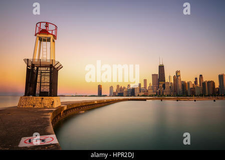 Chicago skyline across Lake Michigan at sunset viewed from North Avenue Beach with a lighthouse in foreground. Long exposure. Stock Photo