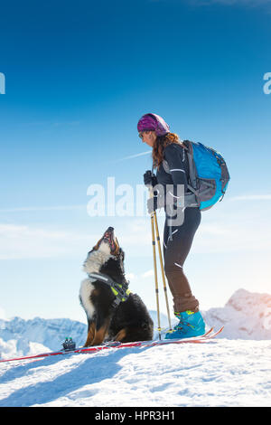 Girl on top of a mountain in winter with skiing and its Bernese dog friend Stock Photo