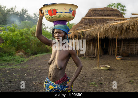 Portrait of a woman from the Holi tribe carrying a load of clothes on her head. She is carrying the load to the nearby stream to wash the clothes. Stock Photo