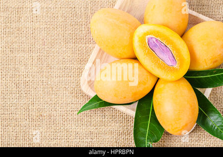 Image of fresh marian plum in wooden dish on sack background. Stock Photo