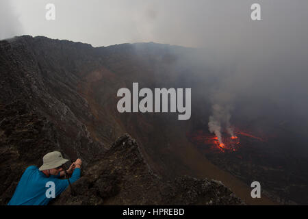 A tourist looks over the crater of Nyiragongo Volcano in the Virunga National Park, DRC to the active lava lake below. Stock Photo