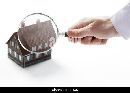 Concept image of a home inspection. A male hand holds a magnifying glass over a miniature house. Stock Photo
