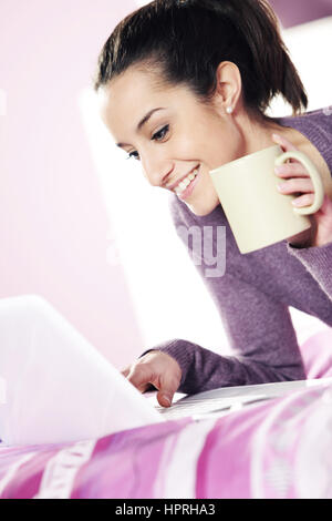 Happy casual  young lady using laptop while lying in bed Stock Photo
