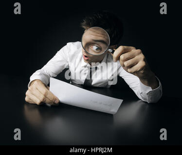 Young businessman looking to a contract through a magnifying glass Stock Photo