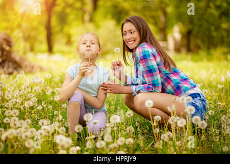 Happy cute little girl blowing dandelion with mother in the park. Stock Photo