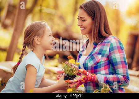Cute smiling little girl assisting her mother planting flowers in a backyard. Stock Photo