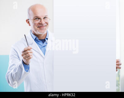 Senior doctor holding a big white sign and pointing with a pen, blank copy space. Stock Photo