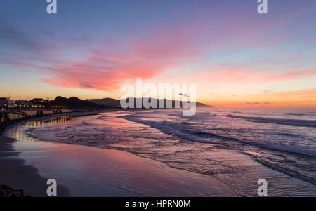 Dunedin, Otago, New Zealand. View over the Pacific Ocean off St Clair Beach at dawn, pink sky reflected in water.