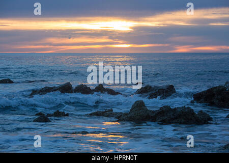 Kaikoura, Canterbury, New Zealand. View across the Pacific Ocean from rocky shoreline at sunrise, golden light reflected in water. Stock Photo