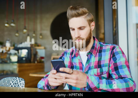 Young man writing on his smartphone in cafe Stock Photo