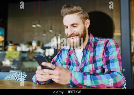 Happy hipster using his smartphone in cafe Stock Photo