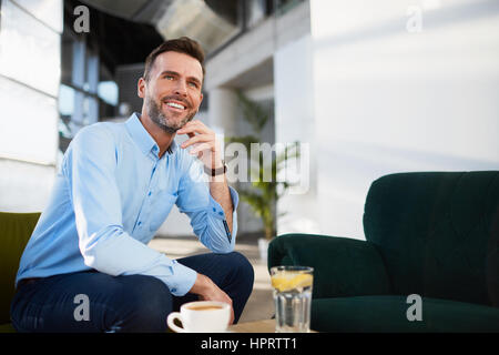 Low angle view of handsome smiling businessman relaxing in office with cup of coffee Stock Photo