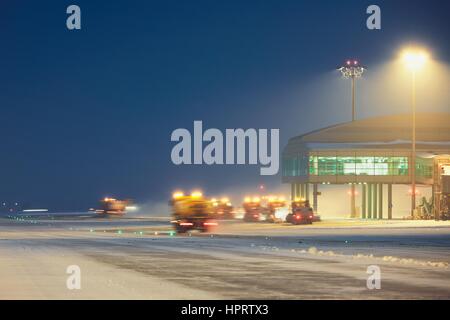 Airport during the snowstorm. Snow plows cleared the snow from the runways and taxiways. - selective focus on terminal building Stock Photo