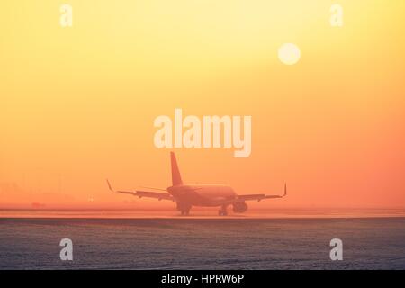 Freezing fog at the airport. Airplane landing during golden sunset. Stock Photo