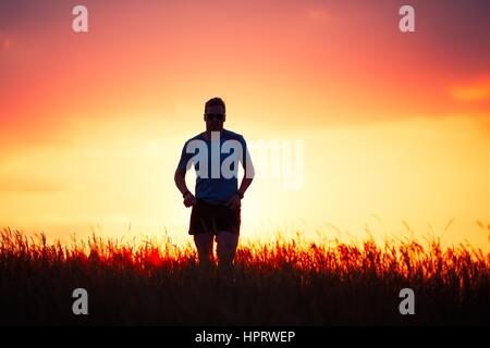 Silhouette of runner. Outdoor cross-country running. Athletic young man is running in the nature during golden sunset. Stock Photo