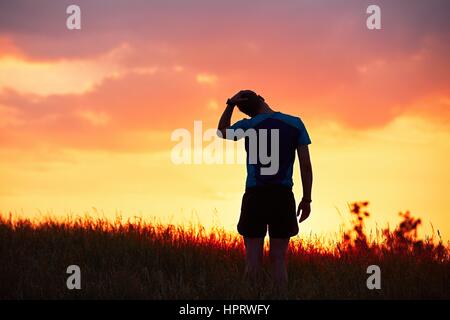 Silhouette of runner. Outdoor cross-country running. Male runner is doing stretching exercise and preparing for workout during golden sunset. Stock Photo