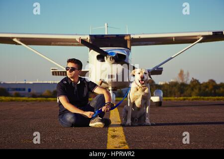 Young pilot with dog are sitting in front of the airplane Stock Photo