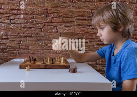 Little caucasian boy playing chess and making next move. Game, education, lifestyle concept Stock Photo