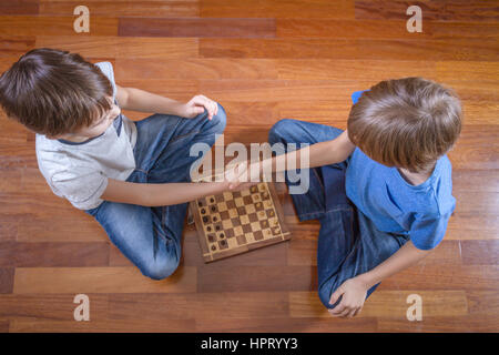 Kids shaking hands before game of chess sitting on wooden floor. Game, education, leisure concept. Top view. Stock Photo