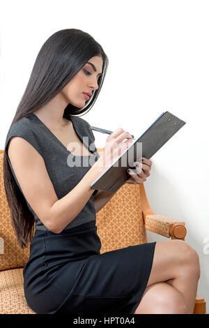 Young business woman sitting while taking notes on a notepad, Stock Photo