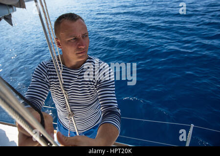 Man holding rope on sailing boat, controlling the sail. Stock Photo