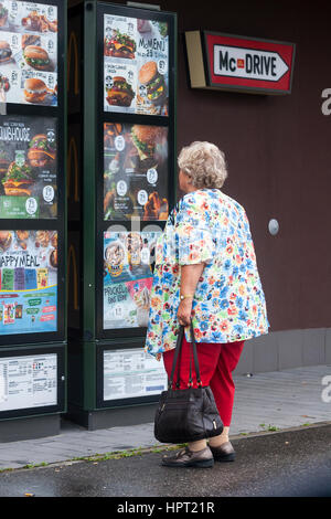 An obese woman looks at the menu outside of the fast-food restaurant in Austria. Stock Photo