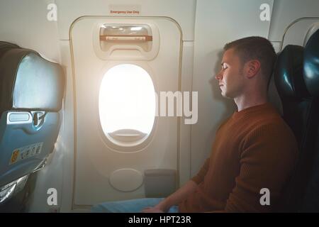 Comfortable traveling by airplane. Young passenger sleeping on the seat near the emergency exit from the aircraft. Stock Photo
