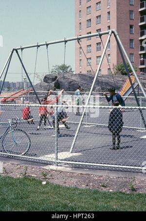 Caucasian and African American children play together on a swing set in a playground outside a public housing project in the Bronx, New York City, New York, 1968. Stock Photo