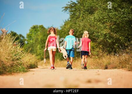 Siblings in nature. Two girls and one boy holding toys and going to play. Stock Photo