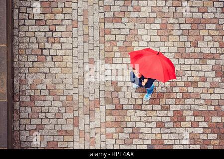 Rainy day. Young man is holding red umbrella and walking in rain. Street of Prague, Czech Republic. Stock Photo