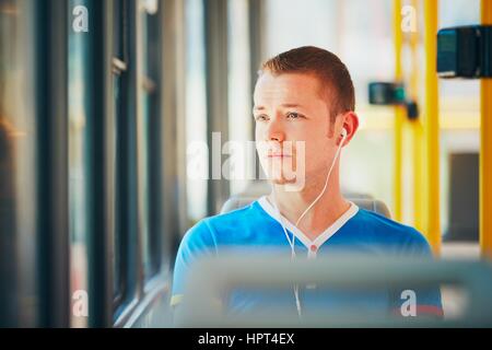 Everyday life and commuting to work by public transportation. Handsome young man is traveling by tram (streetcar). Man is wearing headphones and liste Stock Photo