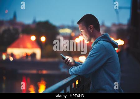 Alone in the night city with mobile phone. Handsome dreamy man reading message (or looking on the video) on his smartphone. Stock Photo