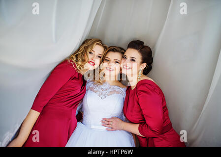 Cute blonde bride with bridesmaids posed on curtains at wedding morning day. Stock Photo