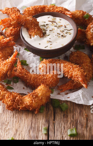 Delicious fried shrimp in coconut chips close-up and cream sauce on the parchment on the table. vertical Stock Photo