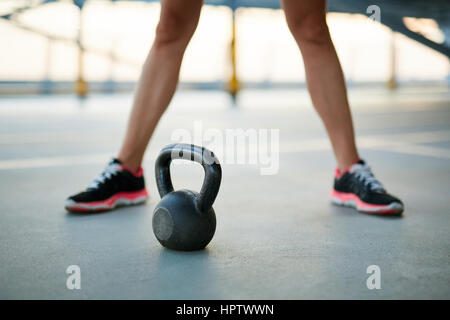 Closeup of woman legs with a kettlebell on a concrete floor of parking garage Stock Photo