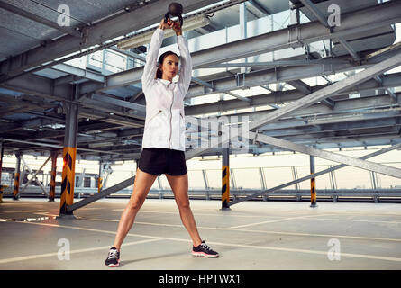 Young woman doing kettlebell swing exercise on parking garage Stock Photo