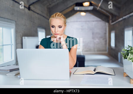 Sad thoughtful business woman working on laptop at modern office Stock Photo