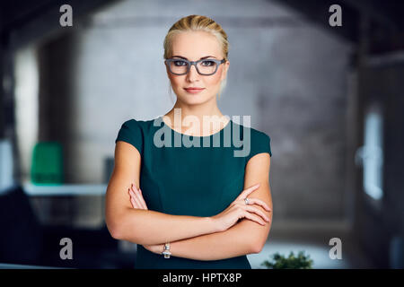 Portrait of confident businesswoman in green dress standing in modern office Stock Photo