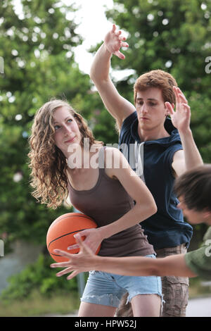 Two boys and a girl playing a game of basketball on an outdoor court. Stock Photo