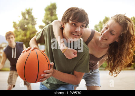 Two boys and a girl playing a game of basketball on an outdoor court. Stock Photo