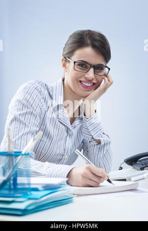 Young attractive businesswoman writing down notes and smiling. Stock Photo