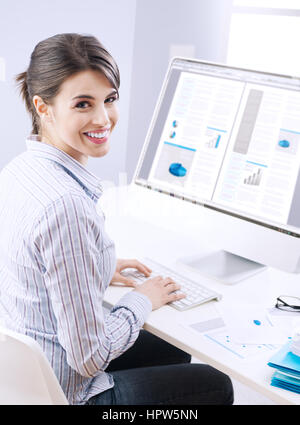 Young office worker smiling and typing on a  keyboard at office. Stock Photo