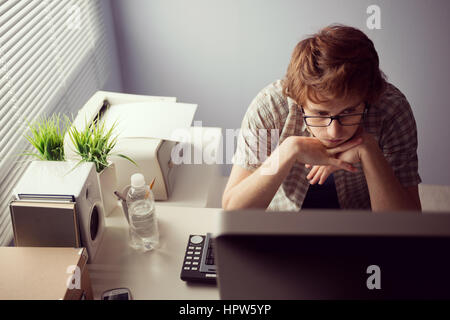 Young bored guy at office staring at computer screen. Stock Photo