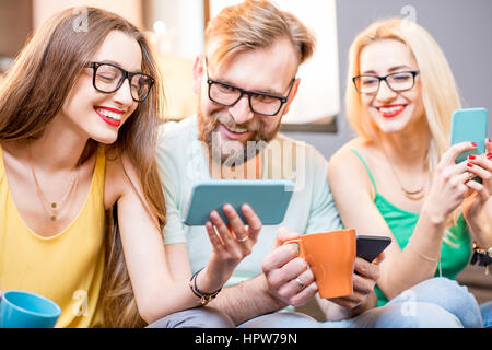 Young friends sitting with smart phones on the couch at home Stock Photo