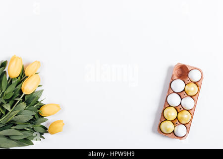 Tray with colored eggs and yellow tulips on a white table top view Stock Photo